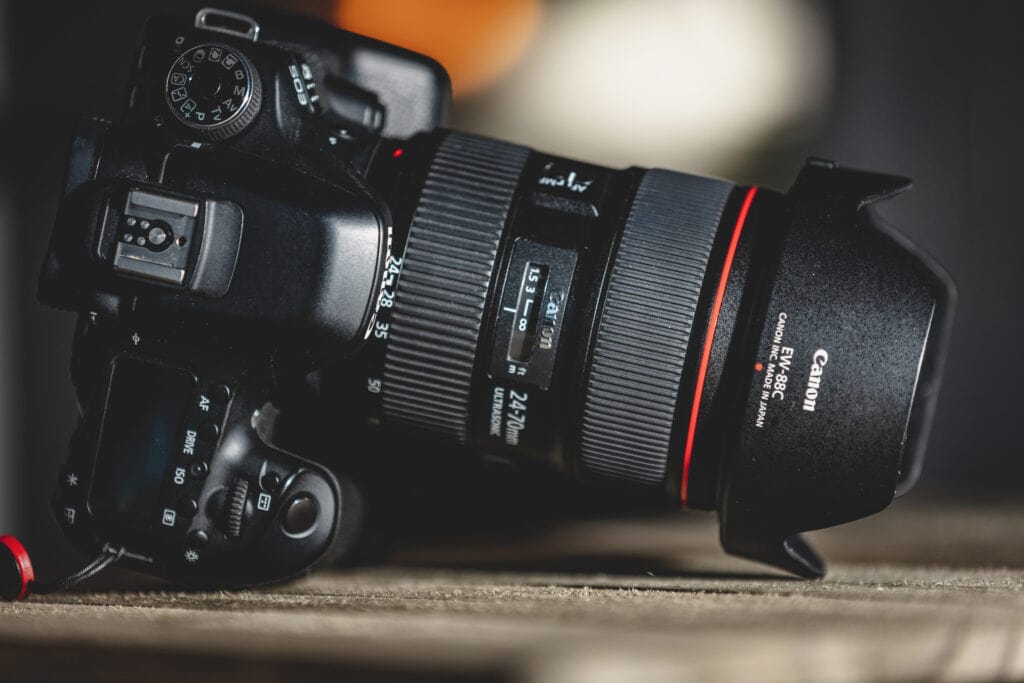Canon DSLR camera with a 24–70mm lens resting on a wooden surface, showing the mode dial and top controls in detail.