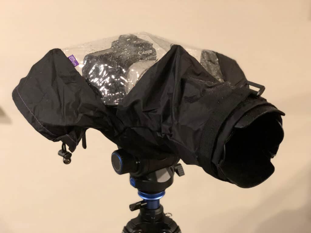 DSLR camera mounted on a tripod and fully enclosed in an Altura rain cover, showing how the protective sleeve shields the camera and lens from wet weather.