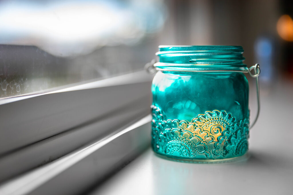 Photo of a small, glass candle holder in a window sill with the lines of the sill pointing to the candle holder.