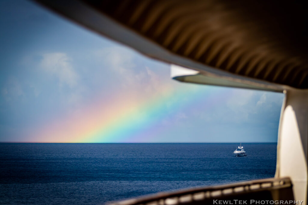 Photo of a rainbow over the ocean framed by the observation deck of a cruise ship.