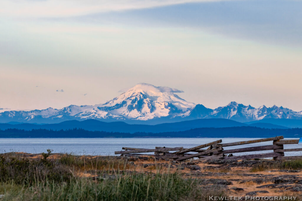 Image of a majestic landscape with a distant mountain, water in the mid-point, and rocky land in the foreground.