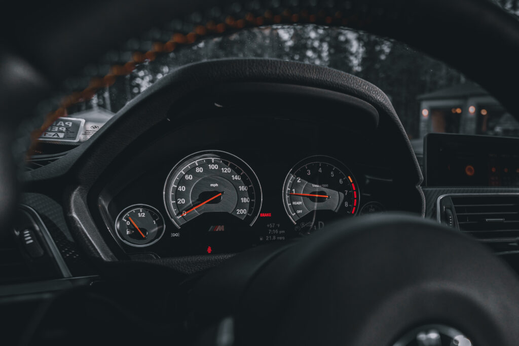 Photo of a speedometer gauge cluster, framed by the steering wheel in a car.