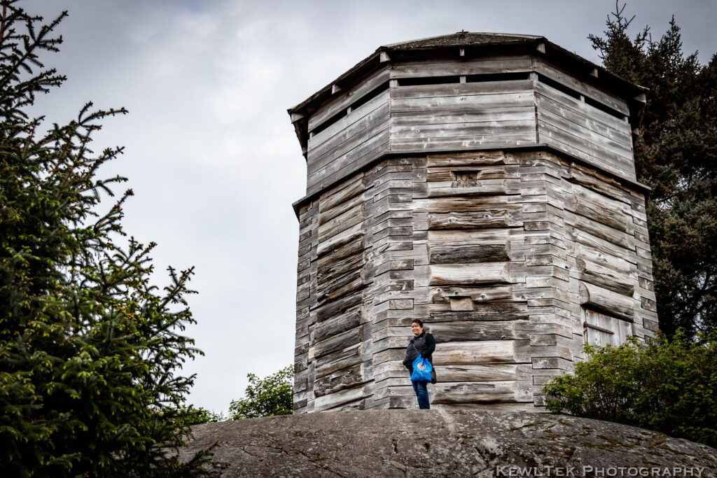 Photo of the historic Russian Blockhouse in Sitka, Alaska with a woman standing next to it in order to show scale.