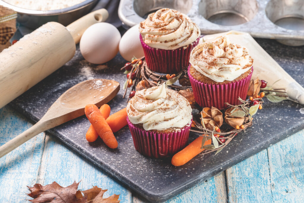 Photo of carrot cake cupcakes surrounded by various baking implements and ingredients, to help tell the story of how the cupcakes were made.