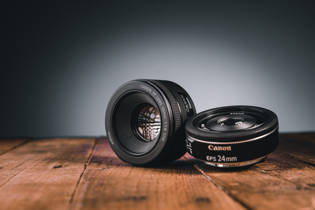 Two Canon prime lenses artistically displayed on a wooden surface.