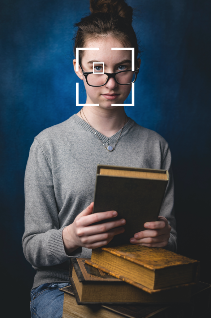 Image of a girl holding books with a camera focus box centered on her face, with an eye detection focus box on her nearest eye.