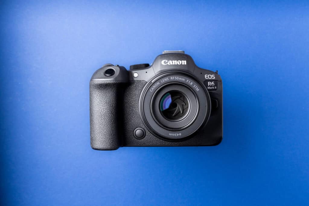Close-up of a Canon mirrorless camera on a bright blue background with a clean, streak-free front lens, illustrating the result after using a microfiber lens cleaning cloth.