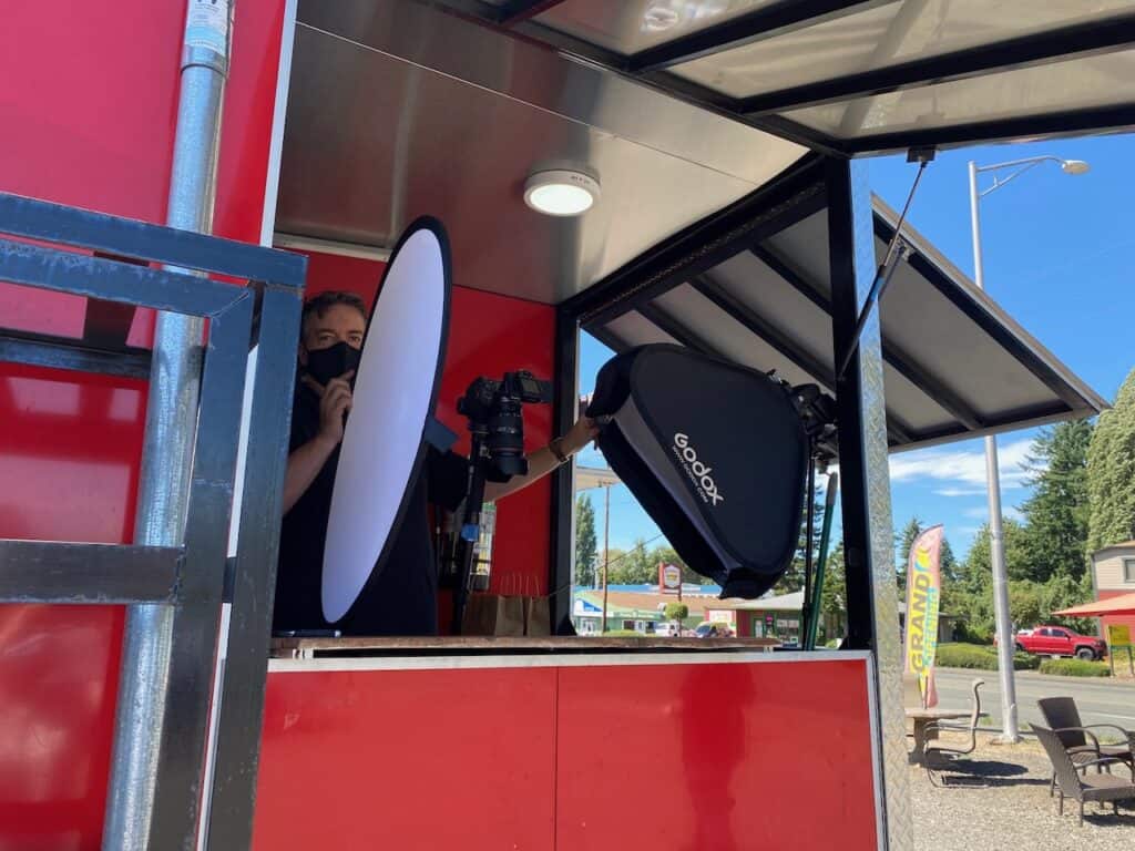 Behind-the-scenes view of a food photography setup at a Thai food trailer, using a Godox V1-C speedlight with light modifiers.