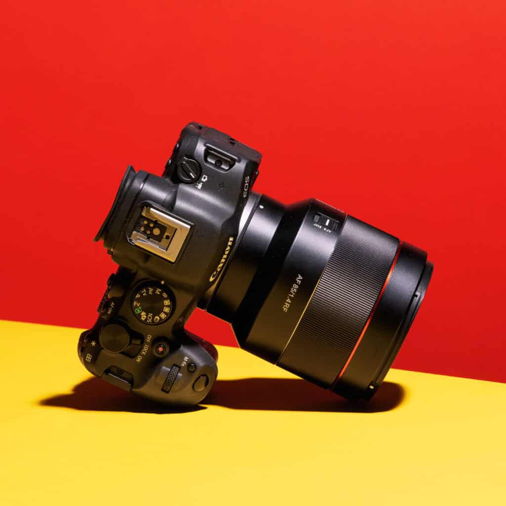 Canon EOS R6 Mark II with a large RF lens photographed on a bold red and yellow background, angled to show the camera’s controls and grip.