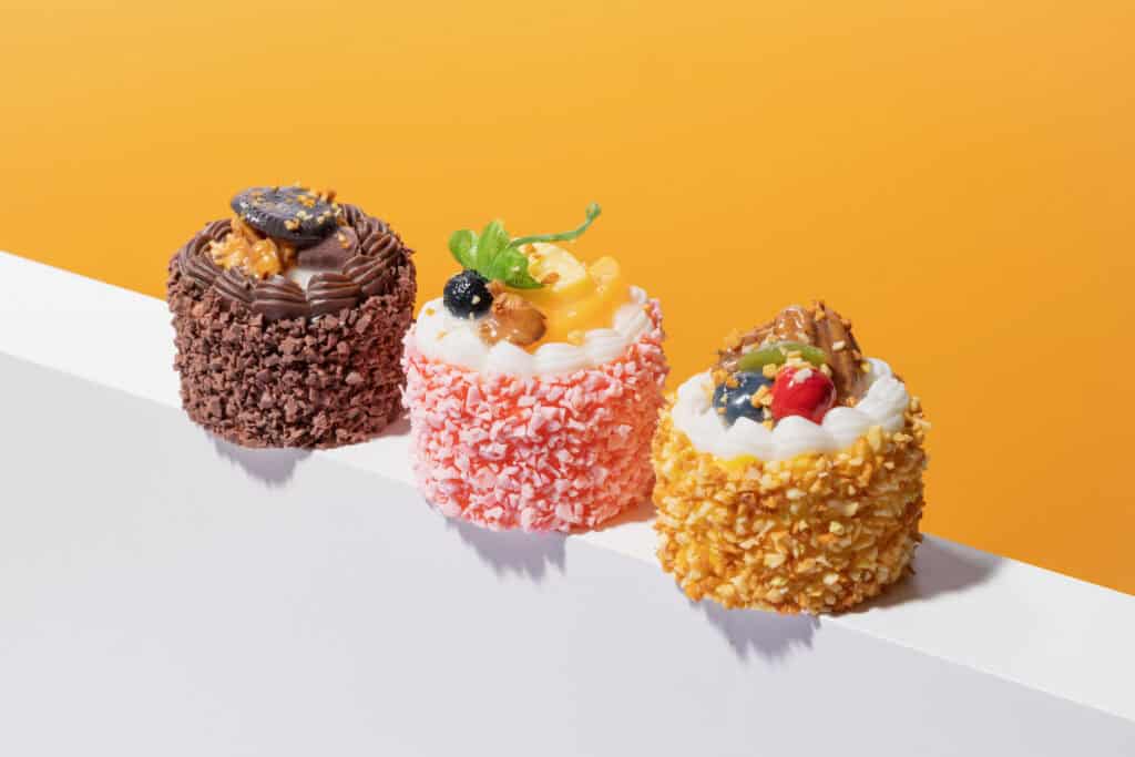 Studio photograph of small dessert cakes arranged on a clean surface, lit with portable strobes for crisp shadows and controlled color.