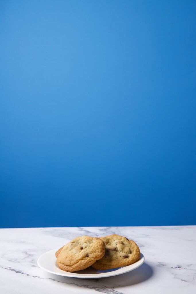 Base setup for the levitation photo showing a white plate with cookies on a marble-style surface against a blue background before compositing.