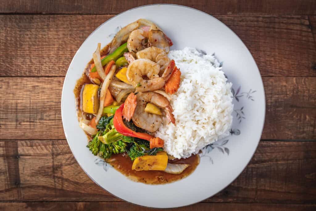 Top-down food photograph of a Thai shrimp dish with vegetables and rice, lit on location using a Godox V1-C speedlight.