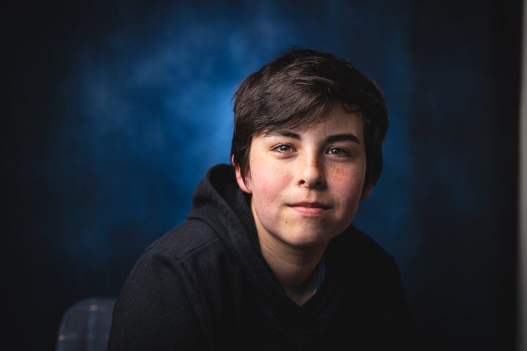 Teen boy photographed indoors using soft directional portrait lighting against a dark blue background