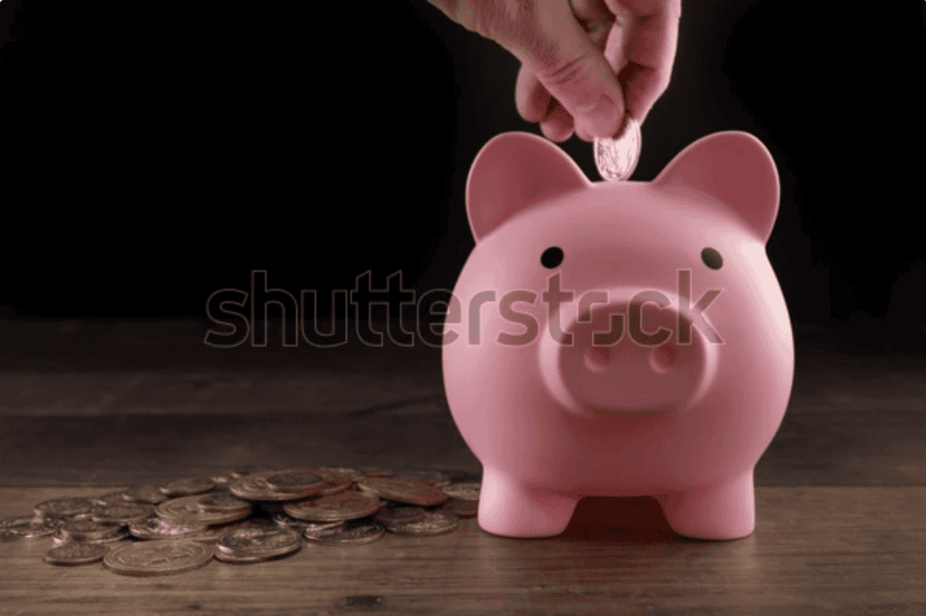 Hand placing a coin into a pink piggy bank on a wooden table